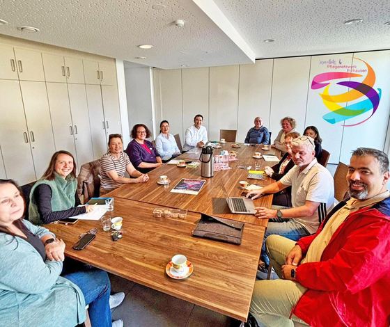 Netzwerktreffen an einem langen Konferenztisch. Rund fünfzehn Personen sitzen mit Unterlagen und Kaffee beisammen, an der Wand das Netzwerklogo. Erzhäuser Gesundheits- und Pflegenetzwerk.