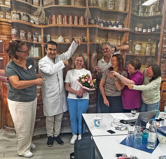 Verabschiedung in der Heegbach Apotheke. Das Team steht vor den alten Apothekenschränken, eine Kollegin hält einen Blumenstrauß. Erzhäuser Gesundheits- und Pflegenetzwerk.