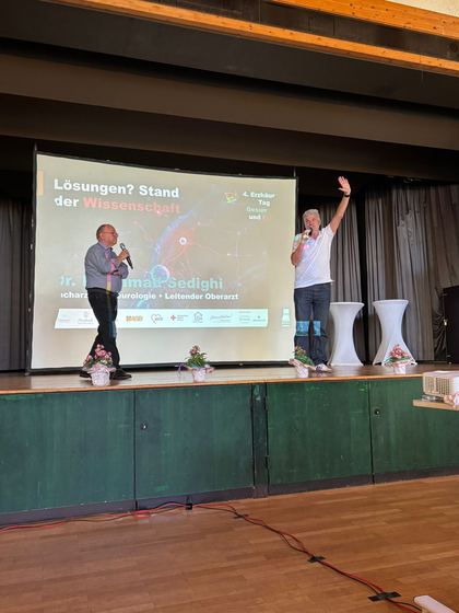 Zwei Referenten auf der Bühne, auf der Leinwand die Folie Lösungen und Stand der Wissenschaft. 4. Erzhäuser Gesundheits- & Pflegetag Erzhausen 2026.