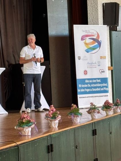 Moderation auf der Bühne, davor eine Reihe kleiner Blumentöpfe. 4. Erzhäuser Gesundheits- & Pflegetag Erzhausen 2026.