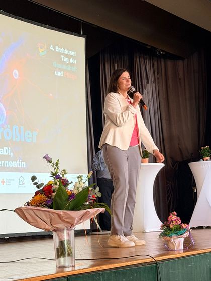 Grußwort auf der Bühne, die Rednerin steht neben einem Blumengesteck. 4. Erzhäuser Gesundheits- & Pflegetag Erzhausen 2026.