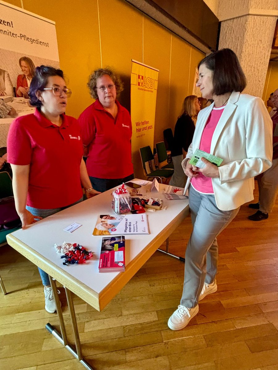 Zwei Mitarbeiterinnen des Johanniter-Pflegedienstes in roten Poloshirts sprechen an ihrem Infotisch mit einer Besucherin. Auf dem Tisch liegen Broschüren zur häuslichen Pflege. 4. Erzhäuser Gesundheits- & Pflegetag Erzhausen 2026.